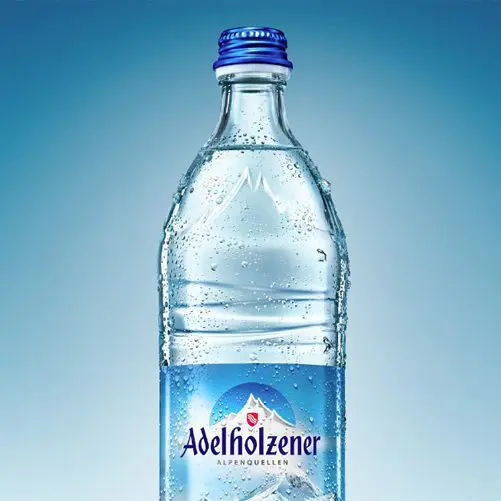 Eine Grafik zeigt eine bläuliche Glasflasche von der Marke Adelholzener vor blauem Hintergrund.