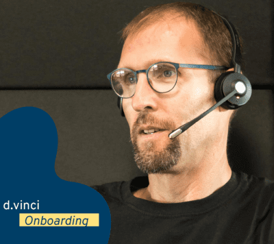 Ein Foto zeigt unseren Kollegen Ivo der ein Headset trägt. Das Bild ist geschmückt mit einer dunkelblauen Welle, dem d.vinci-Logo und dem Text "Onboarding". 